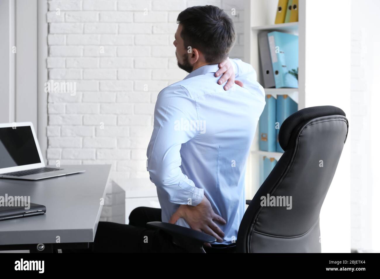 Concetto di postura. Uomo che soffre di mal di schiena mentre lavora con un notebook in ufficio Foto Stock
