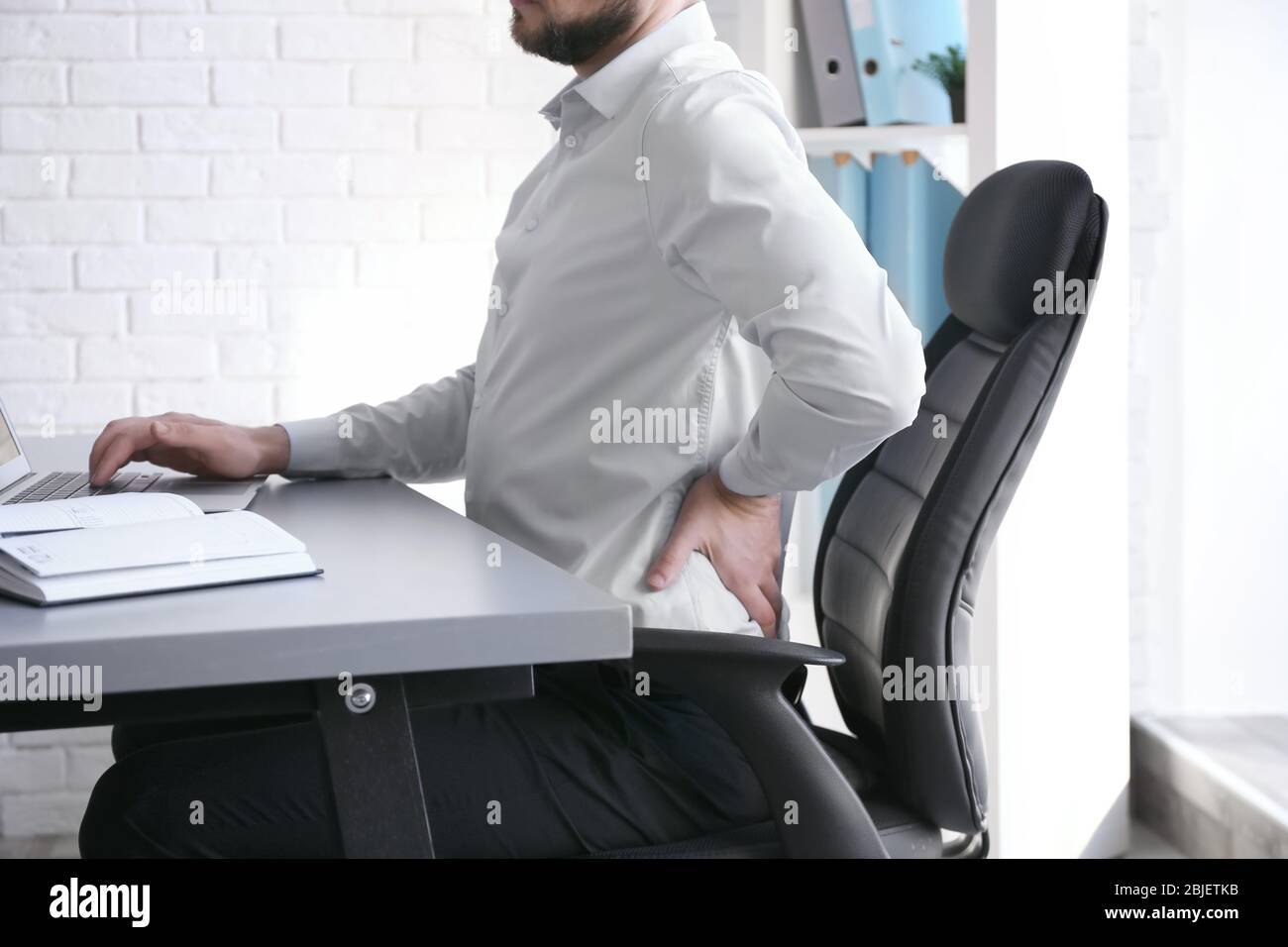 Concetto di postura. Uomo che soffre di mal di schiena mentre lavora con un notebook in ufficio Foto Stock