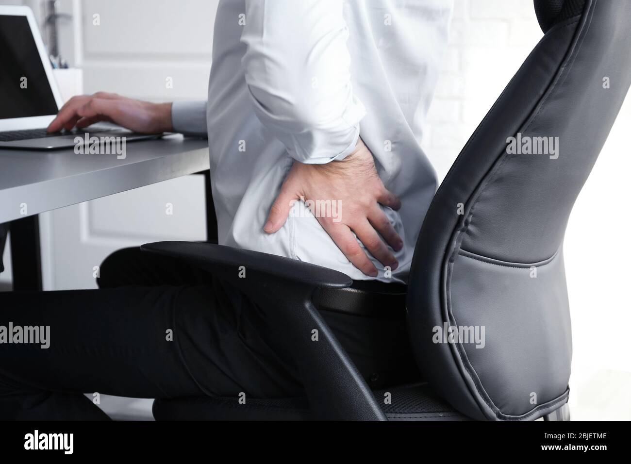 Concetto di postura. Uomo che soffre di mal di schiena mentre lavora con un notebook in ufficio Foto Stock