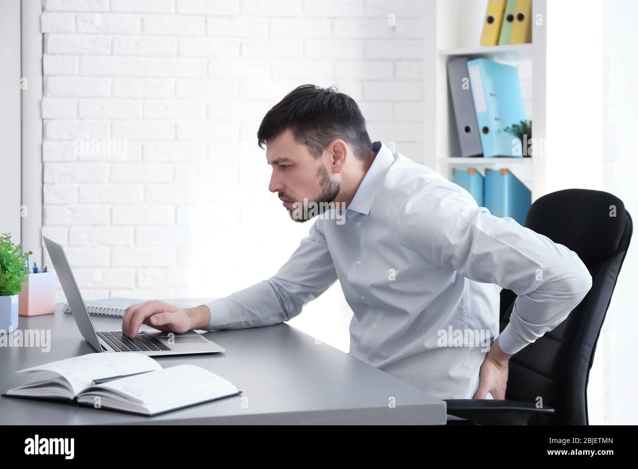 Concetto di postura. Uomo che soffre di mal di schiena mentre lavora con un notebook in ufficio Foto Stock