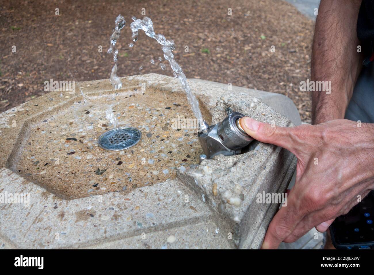 uomo che preme il pulsante per ottenere l'acqua da una fontana pubblica Foto Stock