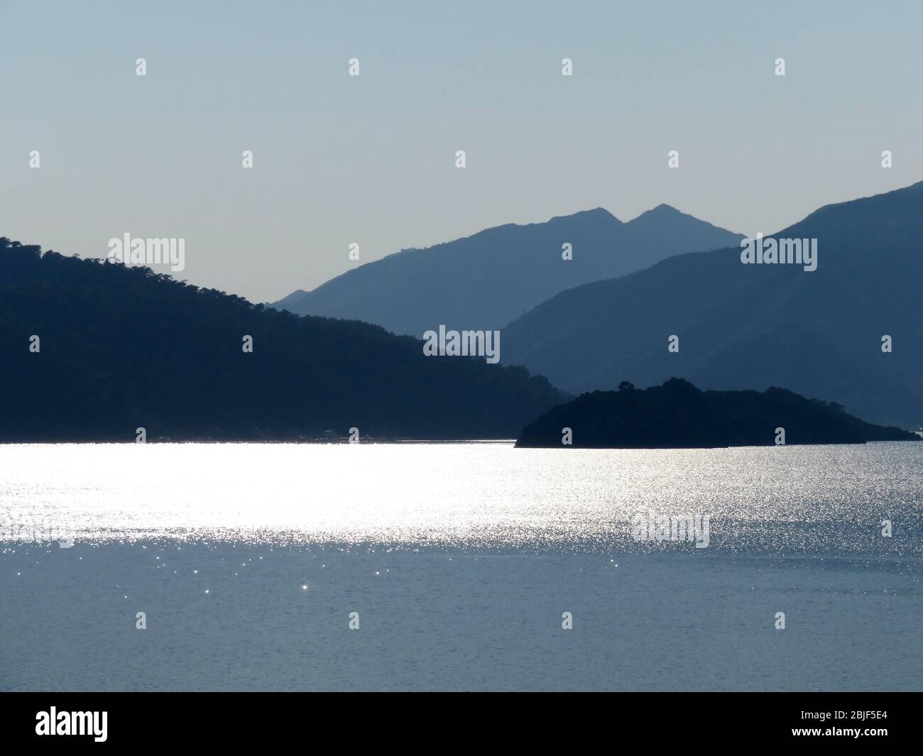 Vista dal mare alle isole montane, costa al mattino presto. Pittoresco mare, costa con colline coperte da foresta in una nebbia Foto Stock