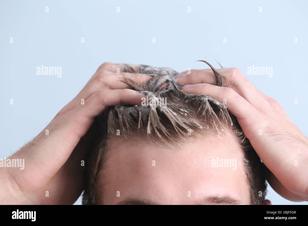 Giovane uomo lavaggio capelli su sfondo colore, closeup Foto Stock