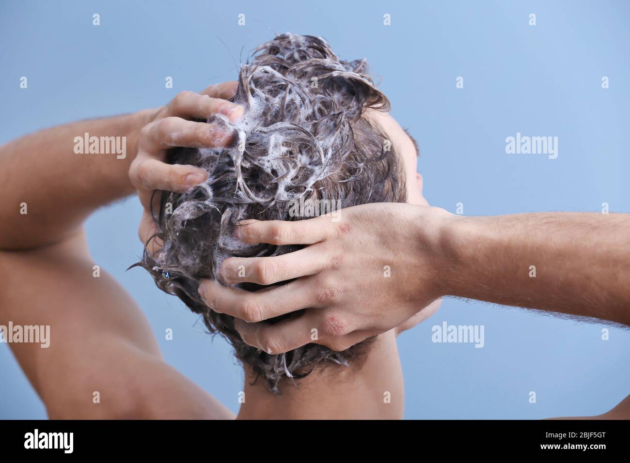 Giovane uomo che lava i capelli su sfondo colore Foto Stock