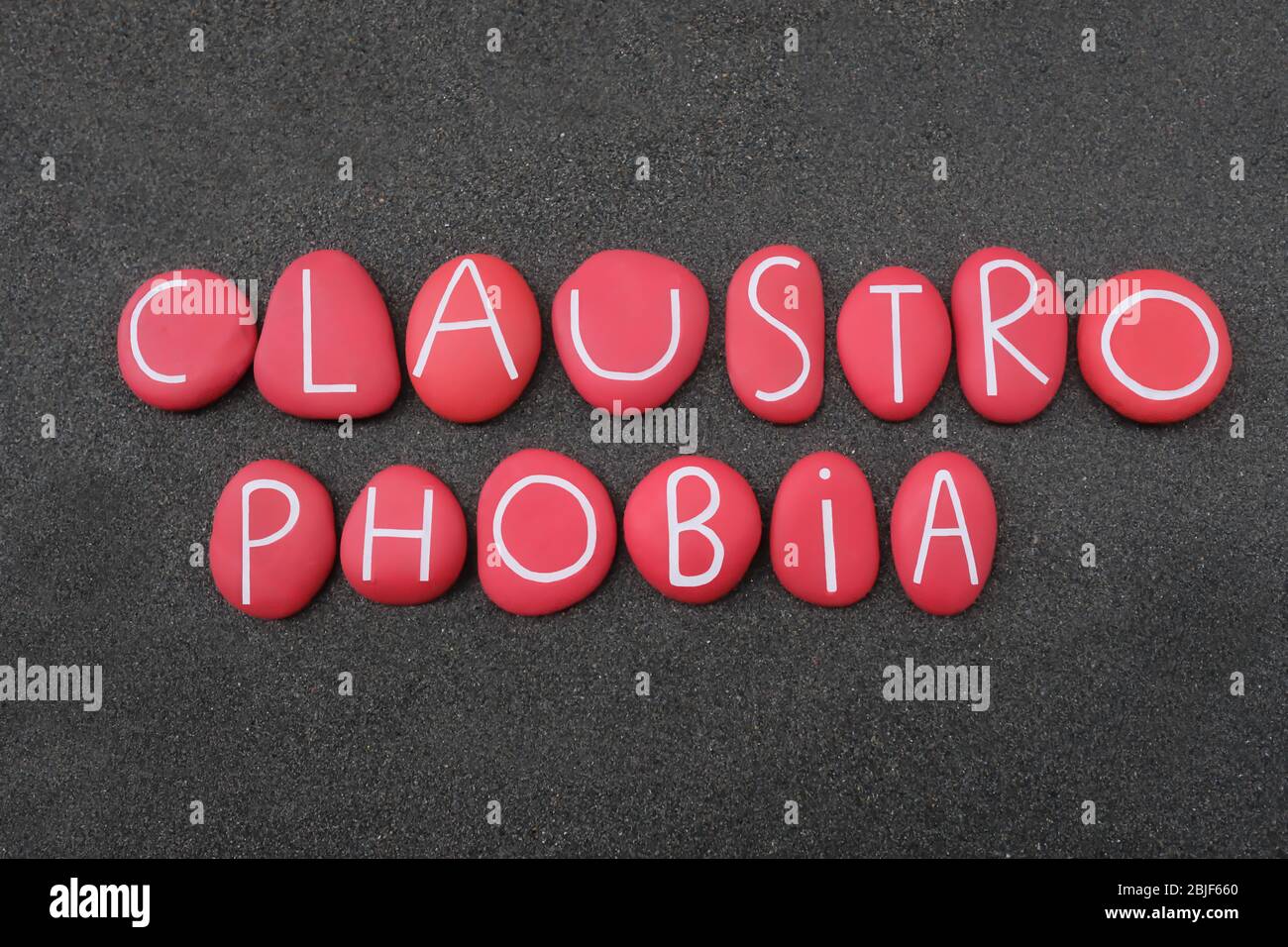Claustrofobia, la paura di spazi ristretti, testo composto da lettere di pietra rossa su sabbia vulcanica nera Foto Stock