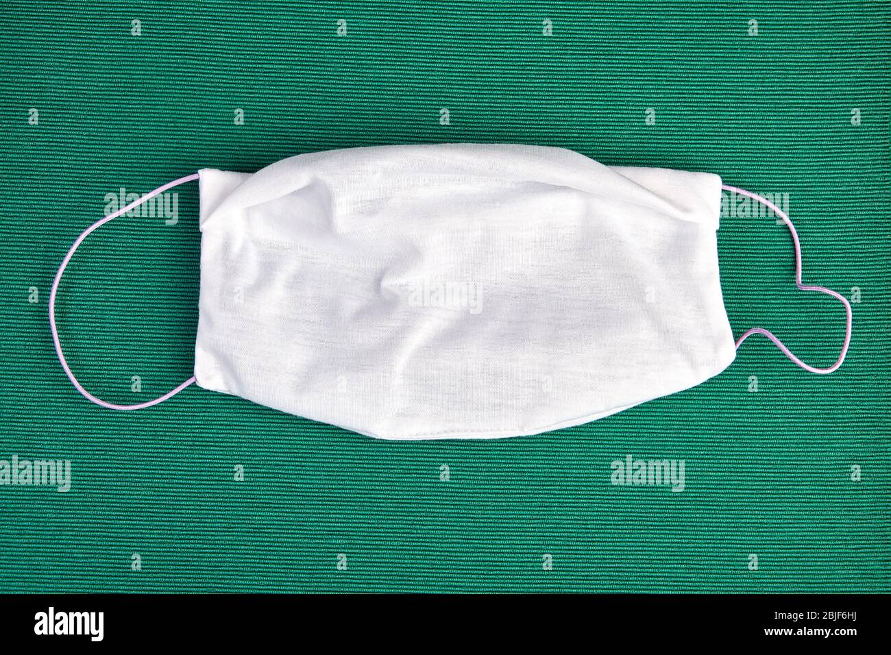 Bendaggio in tessuto o maschera facciale per proteggere il sistema respiratorio durante la pandemia covid-19, su sfondo verde. Maschera facciale in microfibra riutilizzabile, con inature Foto Stock