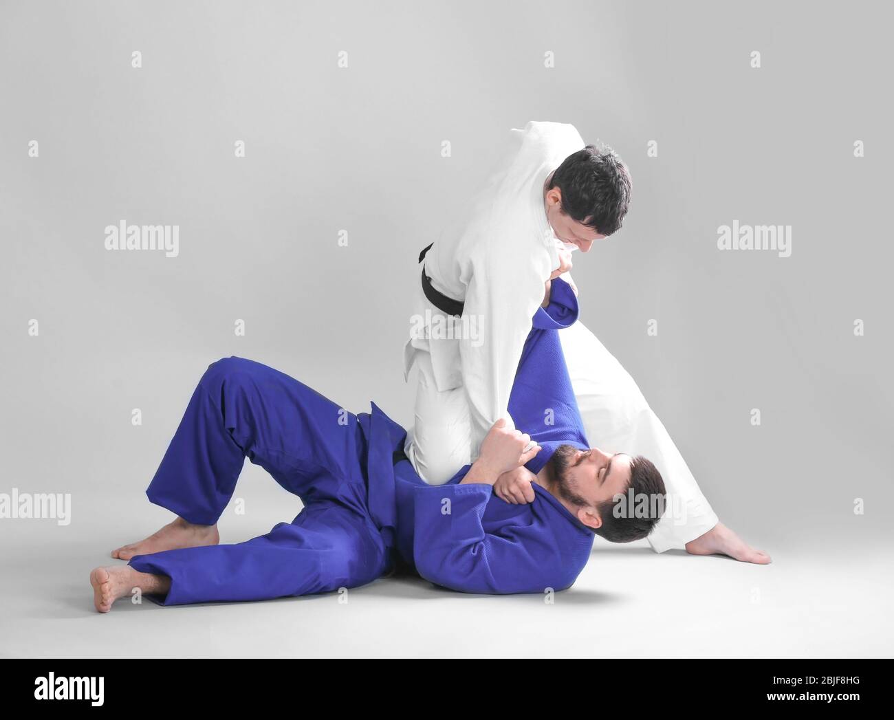 Giovani uomini sportivi che praticano arti marziali su sfondo chiaro Foto Stock