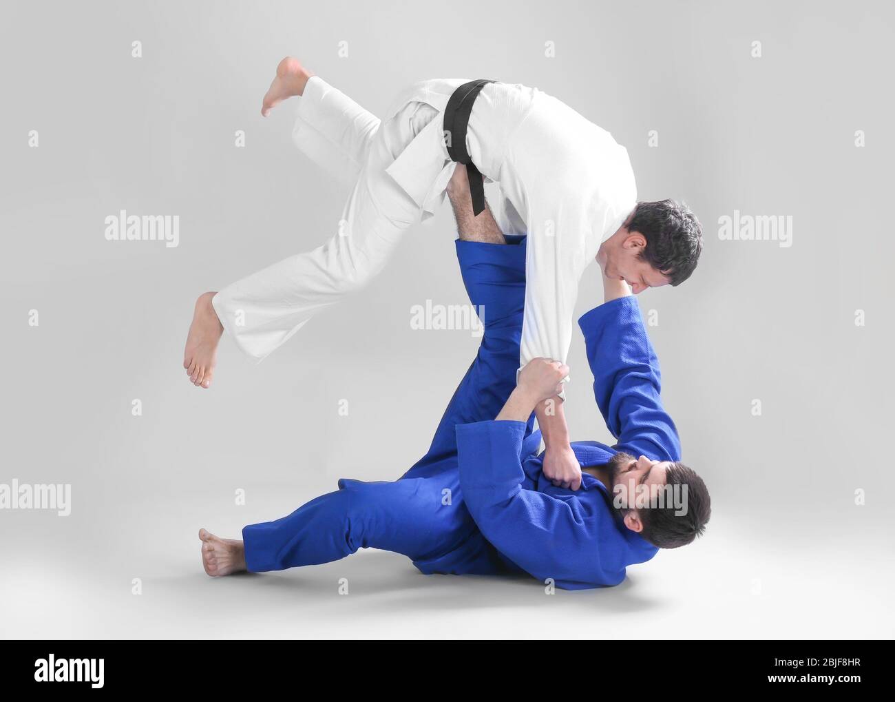 Giovani uomini sportivi che praticano arti marziali su sfondo chiaro Foto Stock