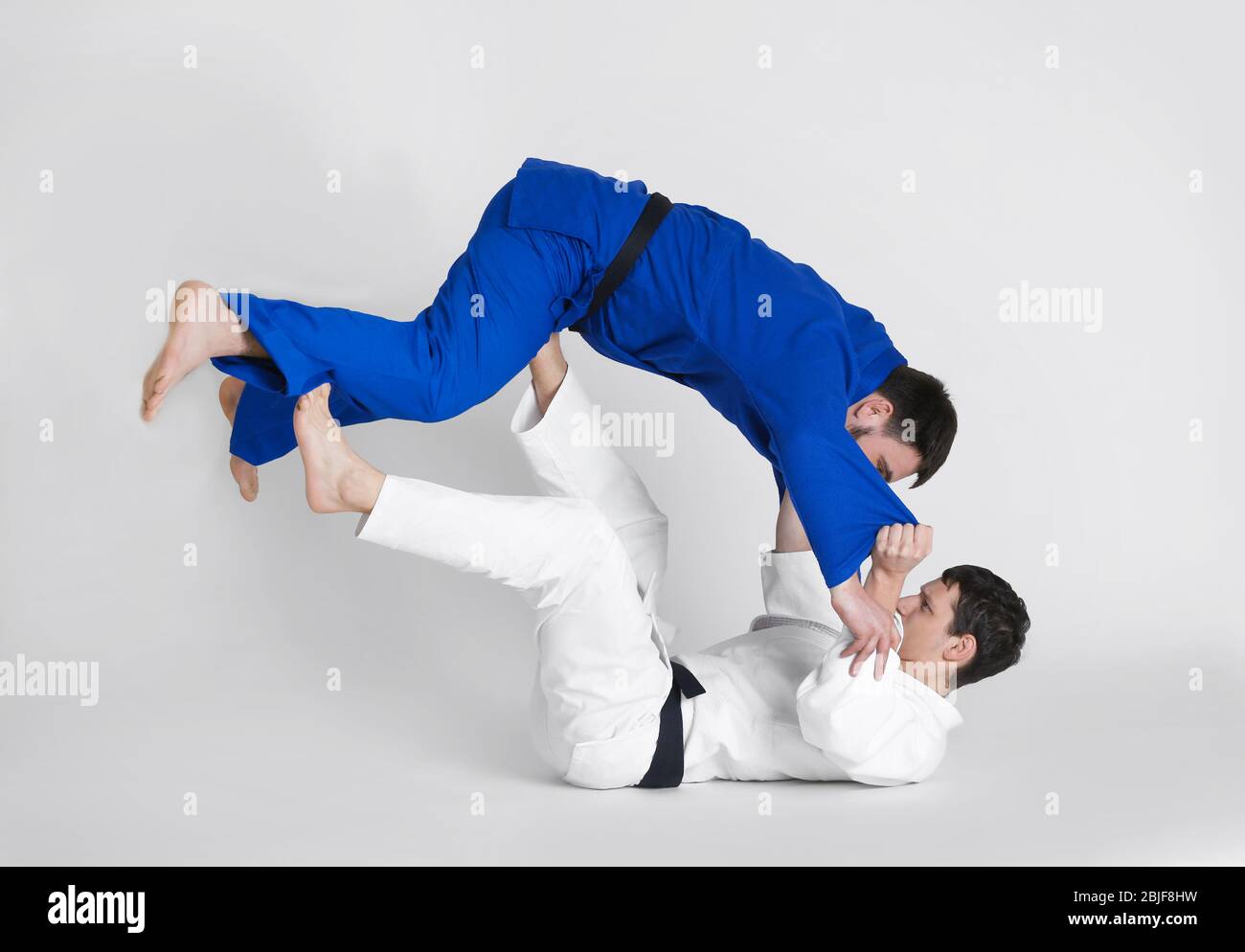 Giovani uomini sportivi che praticano arti marziali su sfondo chiaro Foto Stock