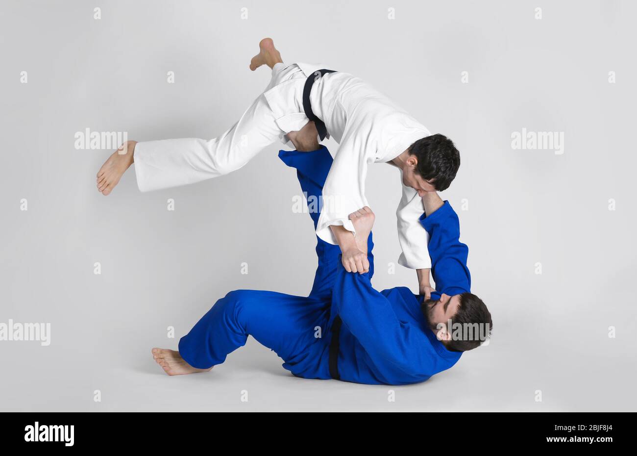 Giovani uomini sportivi che praticano arti marziali su sfondo chiaro Foto Stock