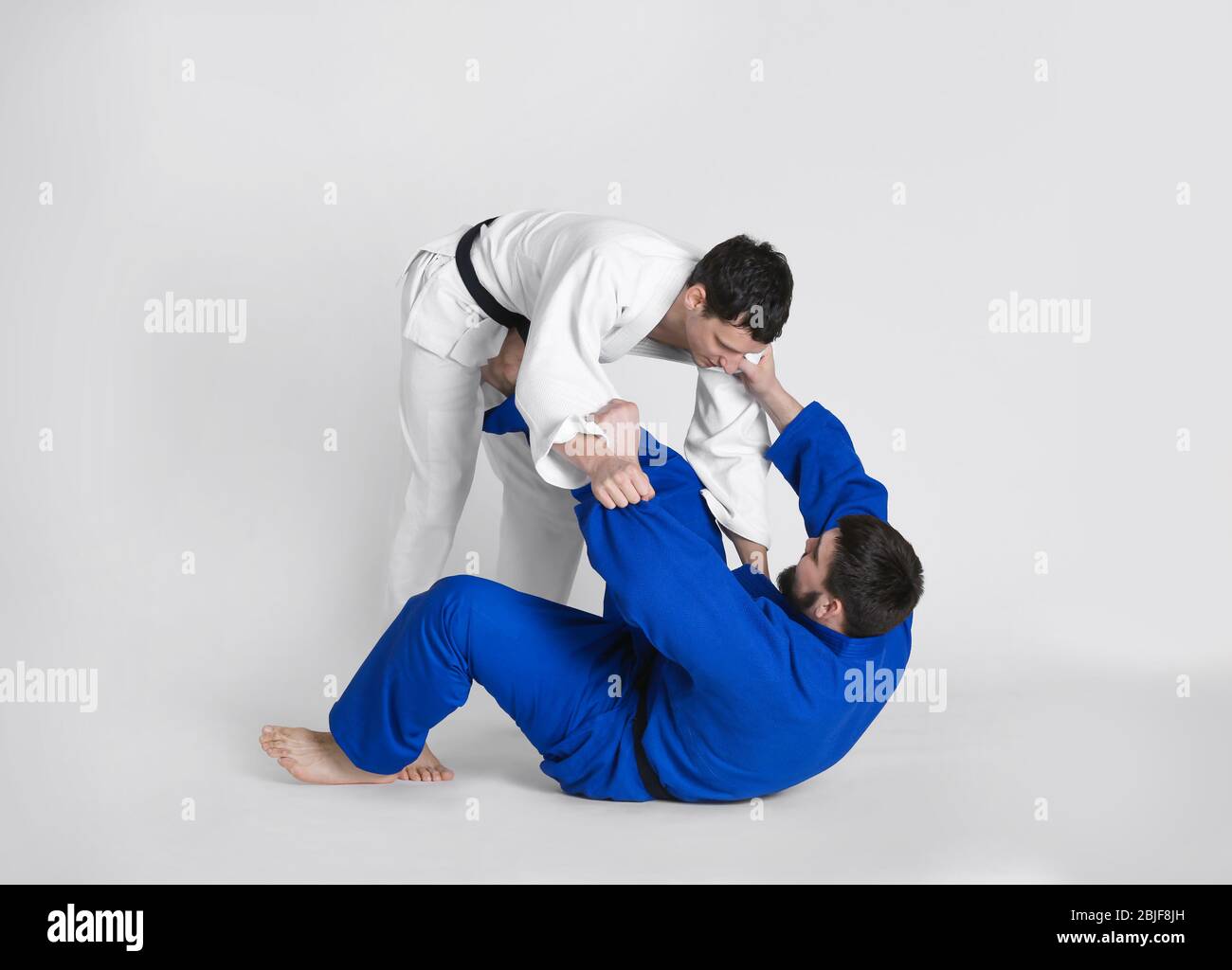 Giovani uomini sportivi che praticano arti marziali su sfondo chiaro Foto Stock