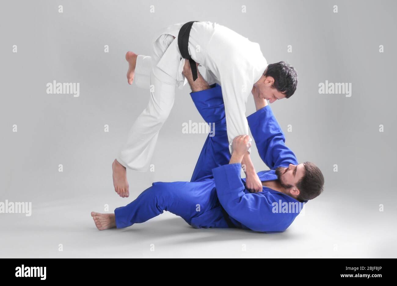 Giovani uomini sportivi che praticano arti marziali su sfondo chiaro Foto Stock