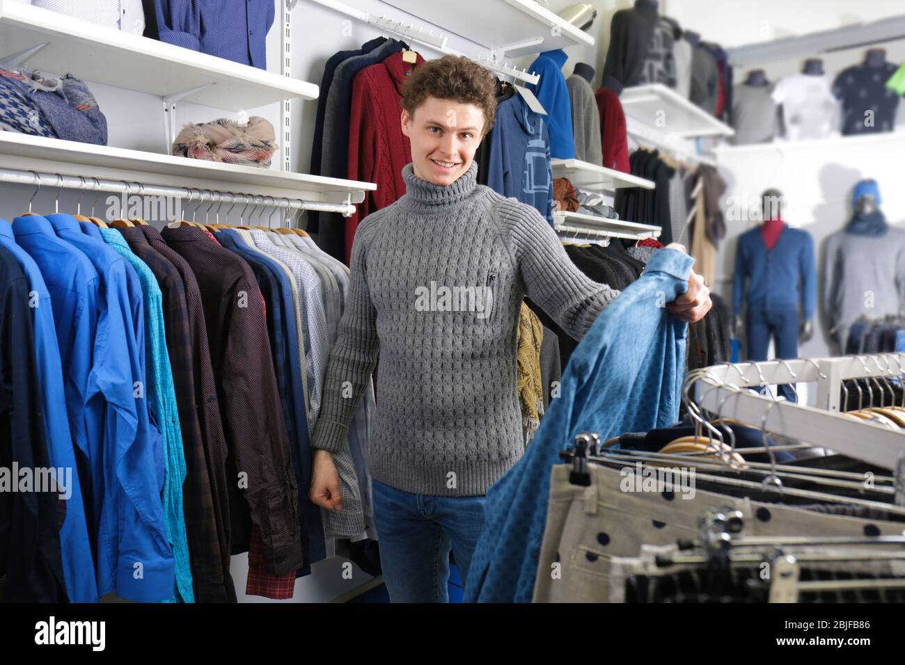 Bel giovane uomo che sceglie vestiti in negozio moderno Foto Stock