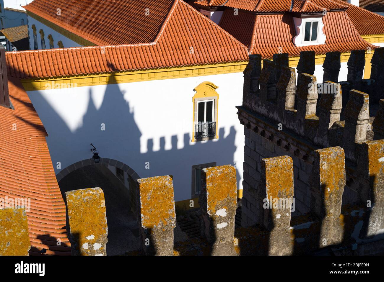 Merlature e ombre della torre della cattedrale se su tipici edifici gialli e bianchi a Evora, Portogallo Foto Stock