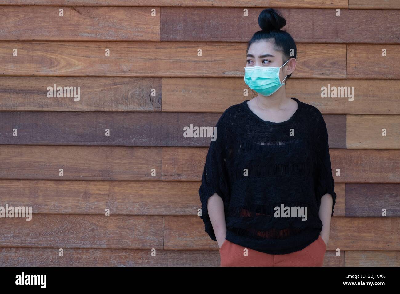 Bella giovane Asia donna che mette su una maschera medica per proteggere dalle malattie respiratorie trasmesse dall'aria come l'influenza covid-19 PM2,5 polvere e smog al woo muro Foto Stock