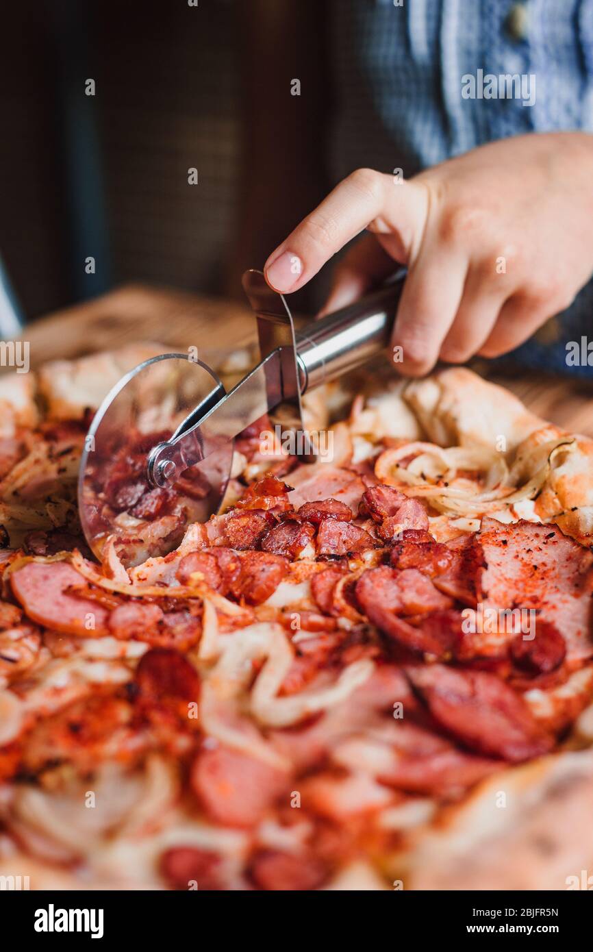 Tagliare la pizza a fette con un coltello speciale. Coltello di supporto manuale. Foto Stock