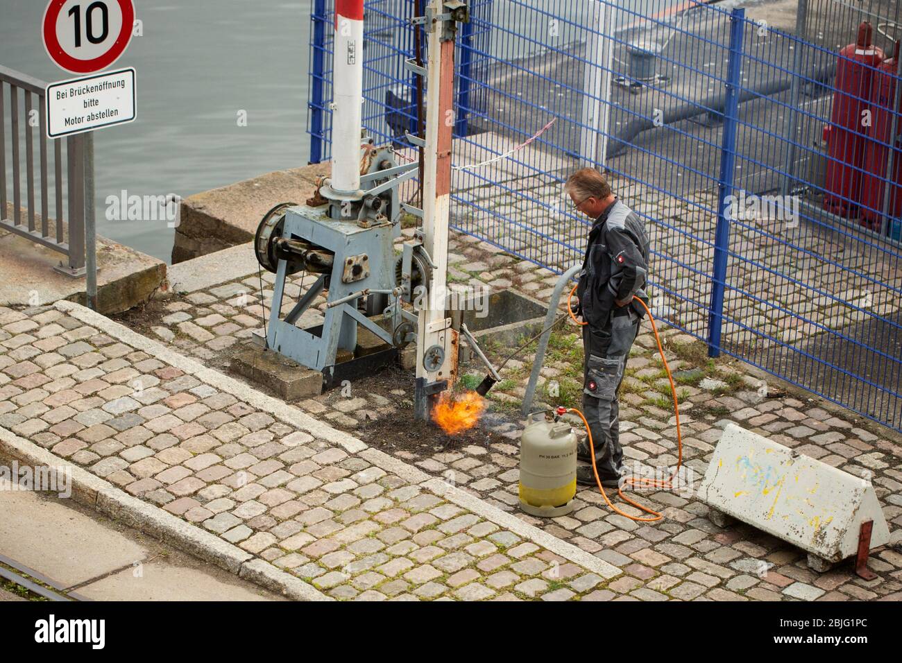 Un operaio utilizza un cannello per distruggere le erbacce nelle prime ore del mattino per le strade di Stralsund, Germania. Foto Stock