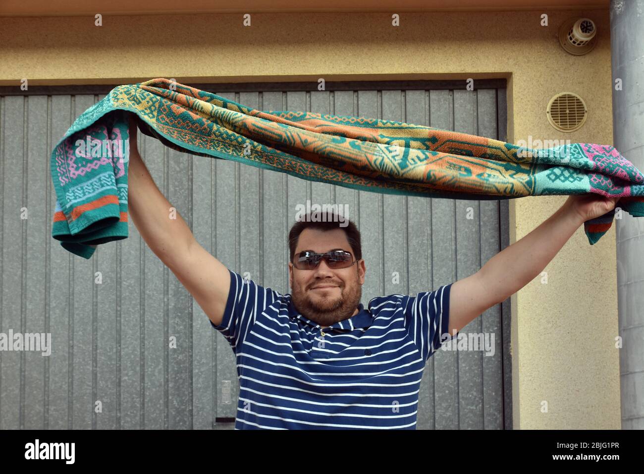 Un uomo con un asciugamano da spiaggia danze sulla terrazza della sua casa per incoraggiare i suoi vicini durante il confinamento tra Crisis.Residents Coronavirus Crisis.Residents di Mas d'en Gual quartiere eseguire e applausi alle 8 pm per incoraggiare i loro vicini durante il confinamento tra la crisi del coronavirus. Ogni giorno scelgono un tema, Musica degli anni '80, Fiera di aprile, oggi hanno fatto uno spettacolo travestito da turisti con le loro valigie e infradito con calze. Foto Stock