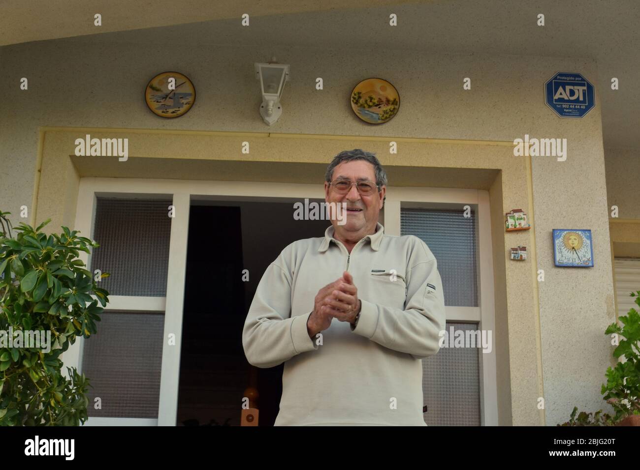 Un uomo applaude i suoi vicini sulla terrazza della sua casa per incoraggiarli durante il confinamento tra Crisis.Residents Coronavirus Crisis.Residents di Mas d'en Gual quartiere eseguire e applausi alle 8 pm per incoraggiare i loro vicini durante il confinamento in mezzo alla crisi del coronavirus. Ogni giorno scelgono un tema, Musica degli anni '80, Fiera di aprile, oggi hanno fatto uno spettacolo travestito da turisti con le loro valigie e infradito con calze. Foto Stock