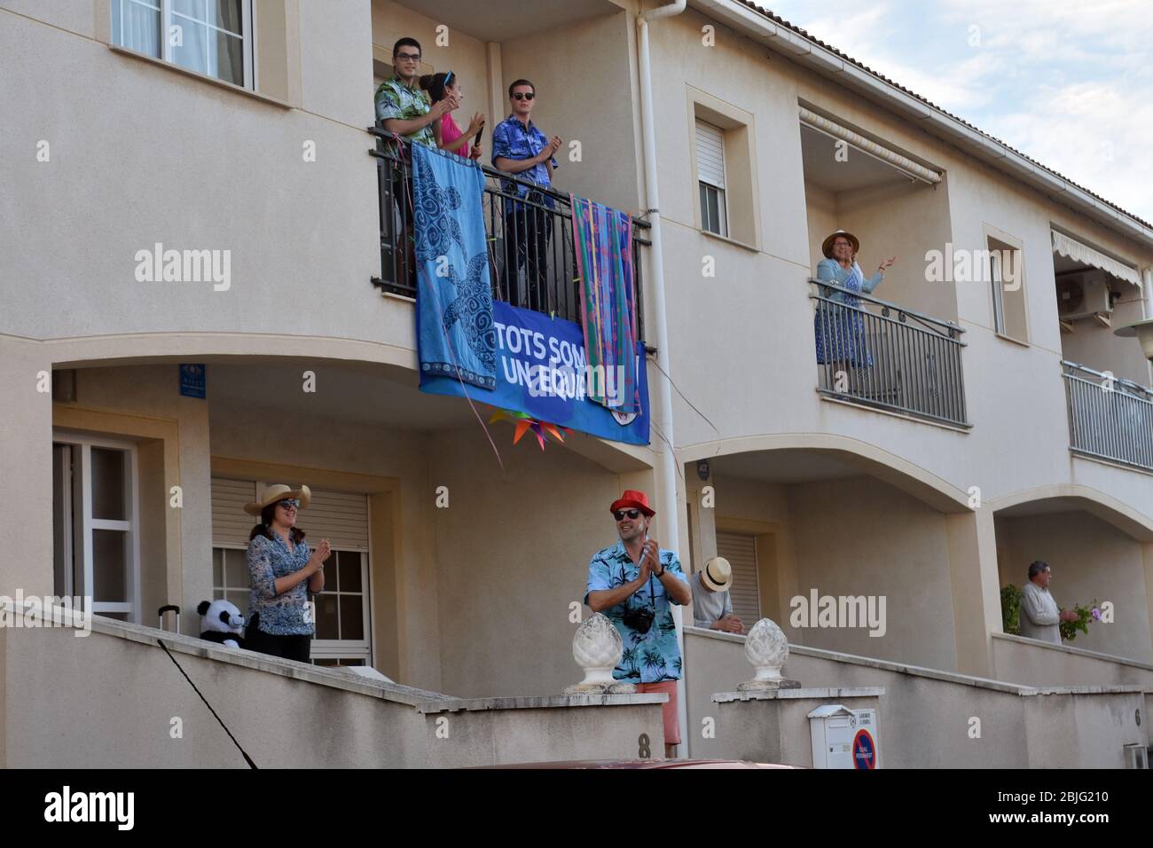 Un gruppo di vicini vestiti come turisti applaudono sulla terrazza delle loro case per incoraggiarsi l'un l'altro durante il confinamento tra Crisis.Residents Coronavirus di Mas d'en quartiere di Gual eseguire e applausi alle 8 pm per incoraggiare i loro vicini durante il confinamento tra la crisi del coronavirus. Ogni giorno scelgono un tema, Musica degli anni '80, Fiera di aprile, oggi hanno fatto uno spettacolo travestito da turisti con le loro valigie e infradito con calze. Foto Stock