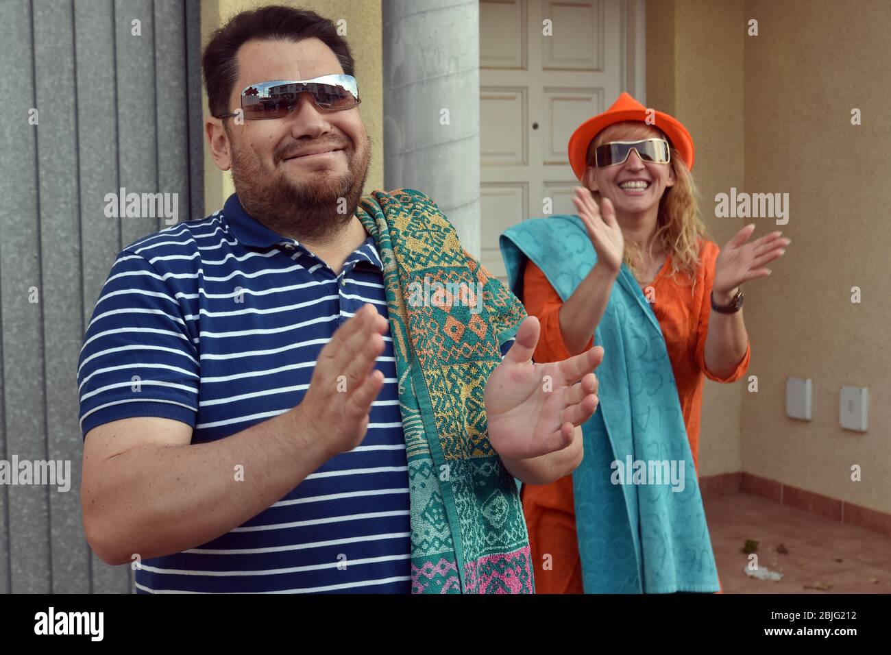 Una coppia con teli da spiaggia mascherati come turisti stranieri applaudono i loro vicini sulla terrazza della loro casa per incoraggiarli durante il confinamento tra Crisis.Residents Coronavirus di Mas d'en quartiere di Gual eseguire e applausi alle 8 pm per incoraggiare i loro vicini durante il confinamento tra la crisi del coronavirus. Ogni giorno scelgono un tema, Musica degli anni '80, Fiera di aprile, oggi hanno fatto uno spettacolo travestito da turisti con le loro valigie e infradito con calze. Foto Stock