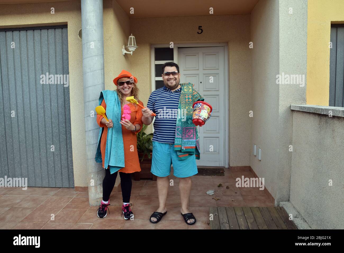 Una coppia con asciugamani tenere bambini accessori spiaggia sulla terrazza della loro casa durante il confinamento tra Crisis.Residents Coronavirus di Mas d'en Gual quartiere eseguire e applausi alle 8 pm per incoraggiare i loro vicini durante il confinamento in mezzo crisi coronavirus. Ogni giorno scelgono un tema, Musica degli anni '80, Fiera di aprile, oggi hanno fatto uno spettacolo travestito da turisti con le loro valigie e infradito con calze. Foto Stock