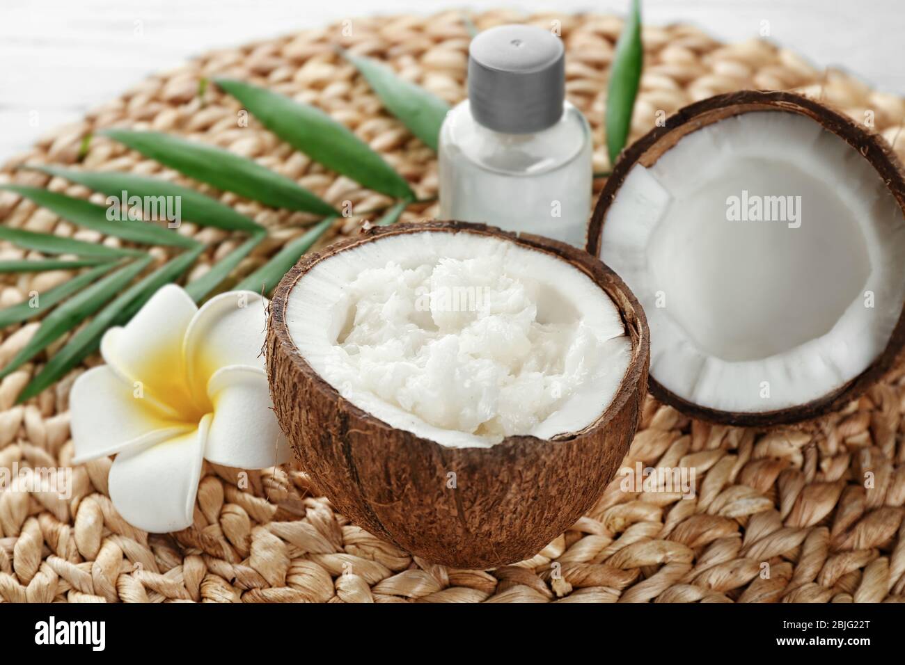 Olio di cocco fresco in metà di noce su tappetino di vimini Foto Stock