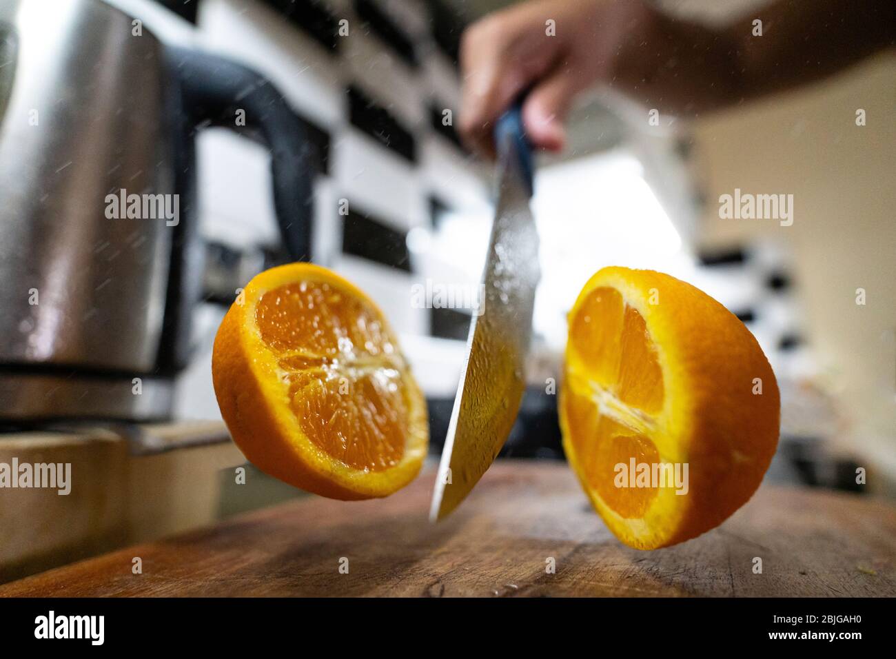 Un taglio arancione a metà con un coltello grande, le due metà apparentemente sospese in aria media. Foto Stock