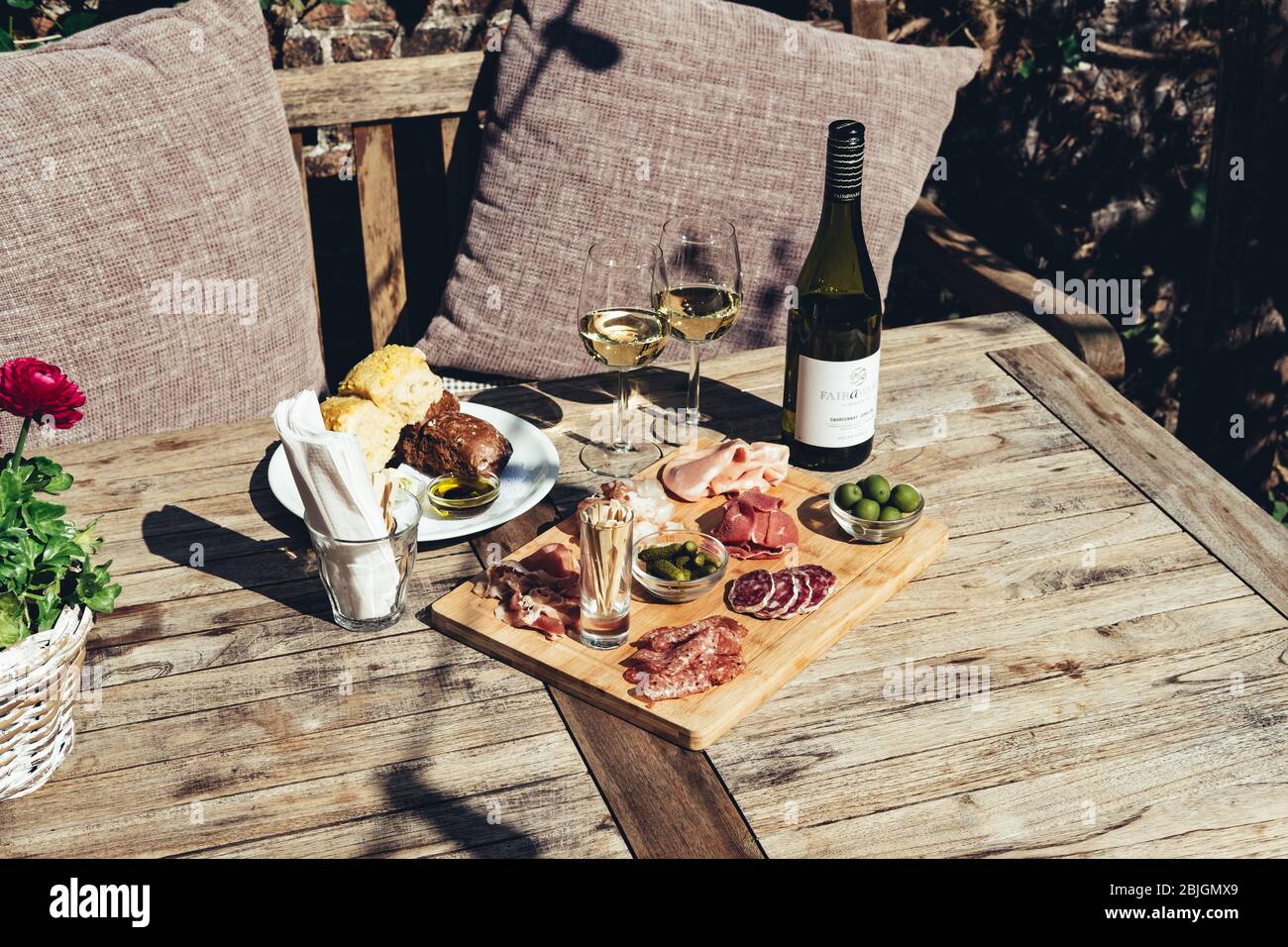 Salumi serviti con vino bianco all'aperto. Un piatto di prosciutto e pancetta affettare con sottaceti su una tavola di legno Foto Stock