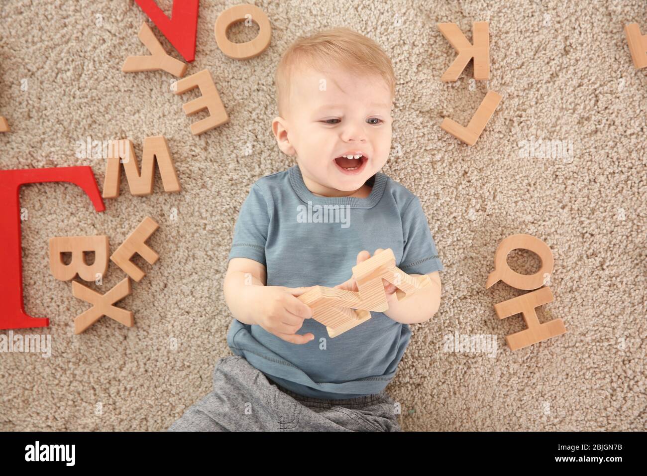 Bambino carino con lettere di legno che giace sul tappeto a casa Foto Stock