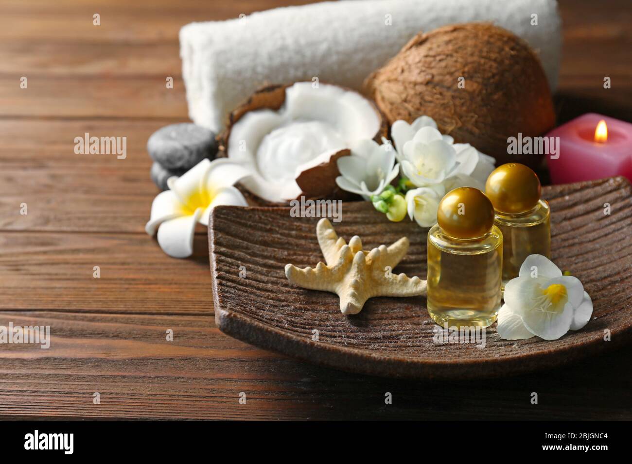 Piatto con olio di cocco in bottiglia, stelle marine e fiori su tavolo di legno Foto Stock