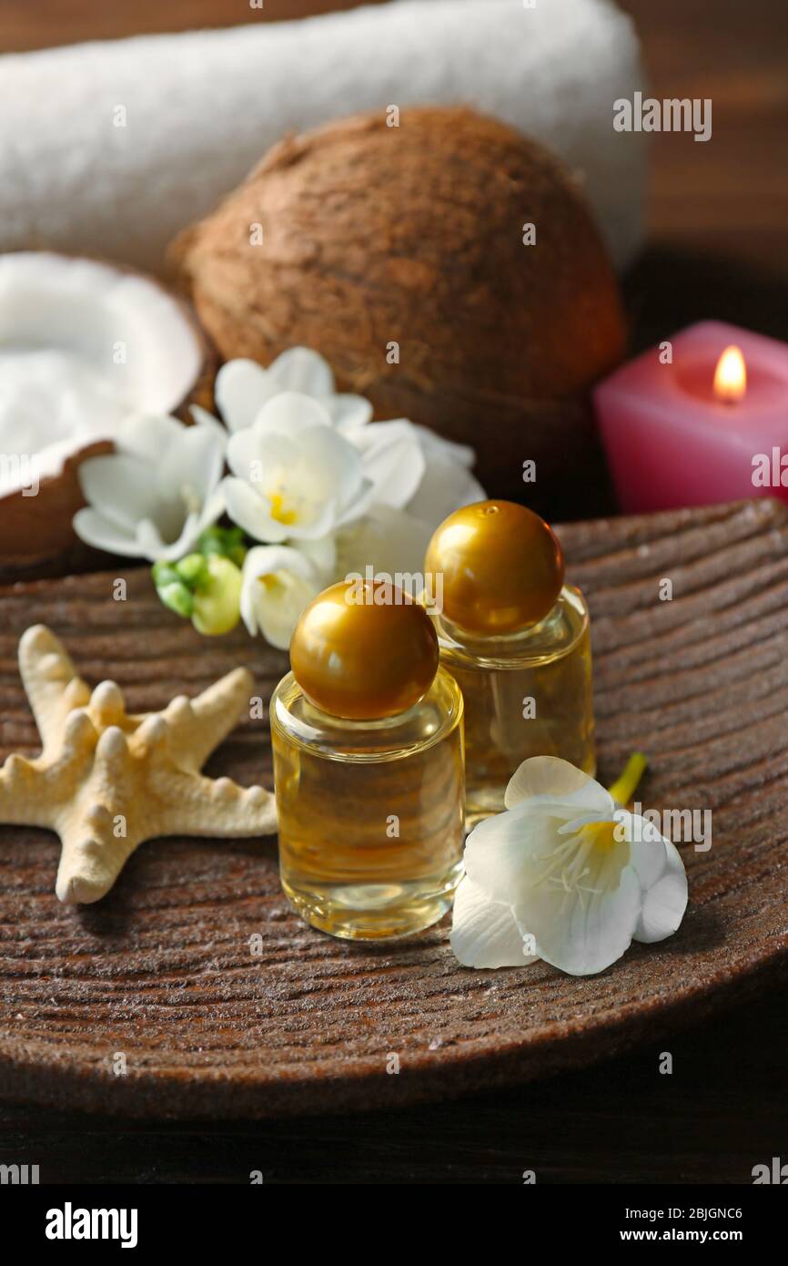 Olio di cocco in bottiglie, stelle marine e fiori su piatto di legno, primo piano Foto Stock