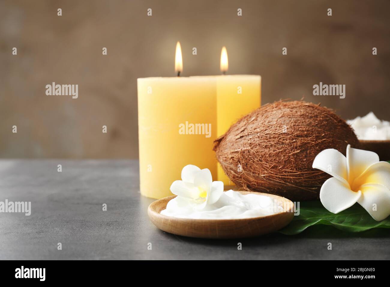Ciotola in legno con crema, cocco e candele su tavolo grigio Foto Stock