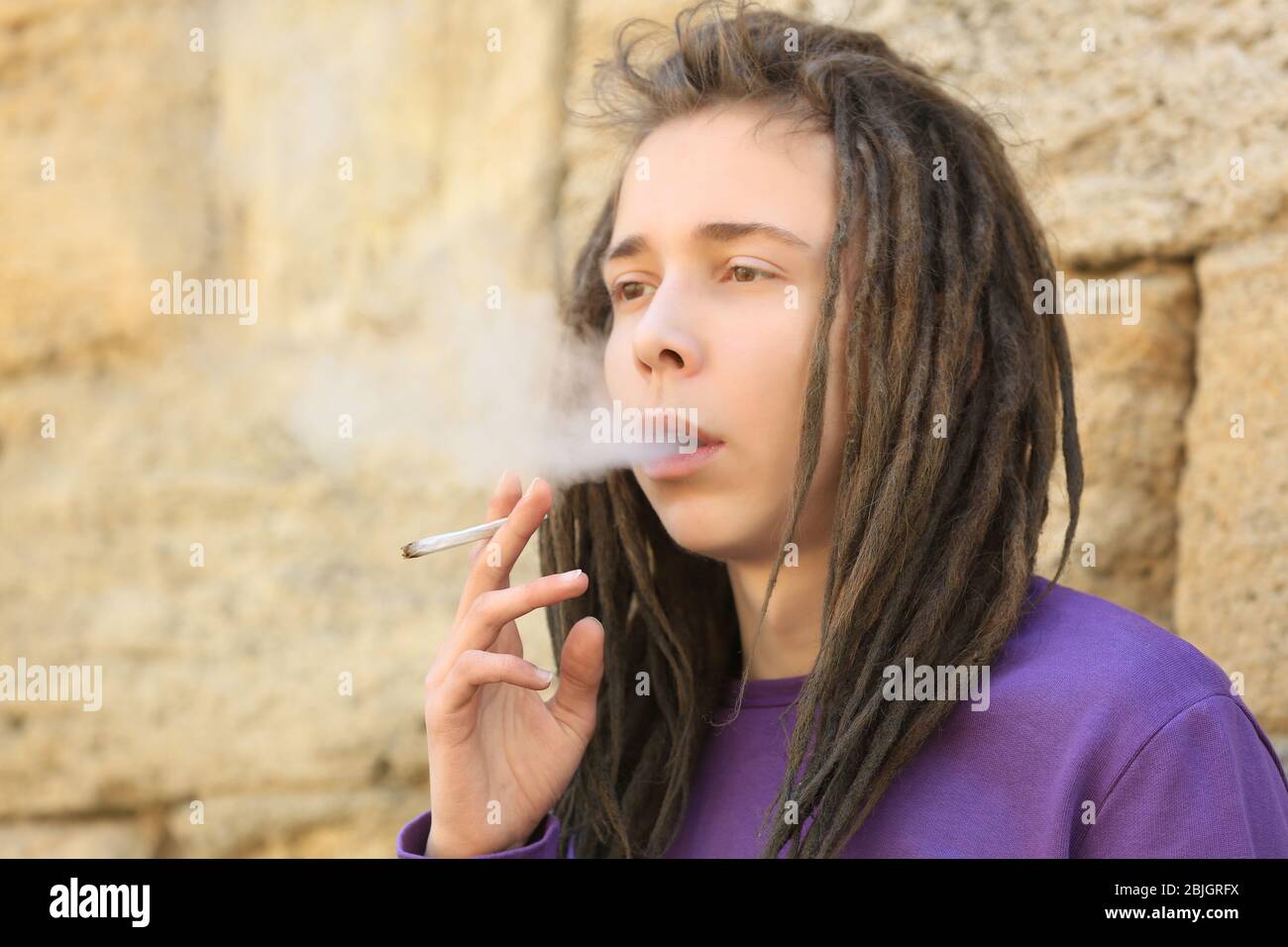 Giovane ragazzo che fuma erbacce su sfondo sfocato Foto Stock