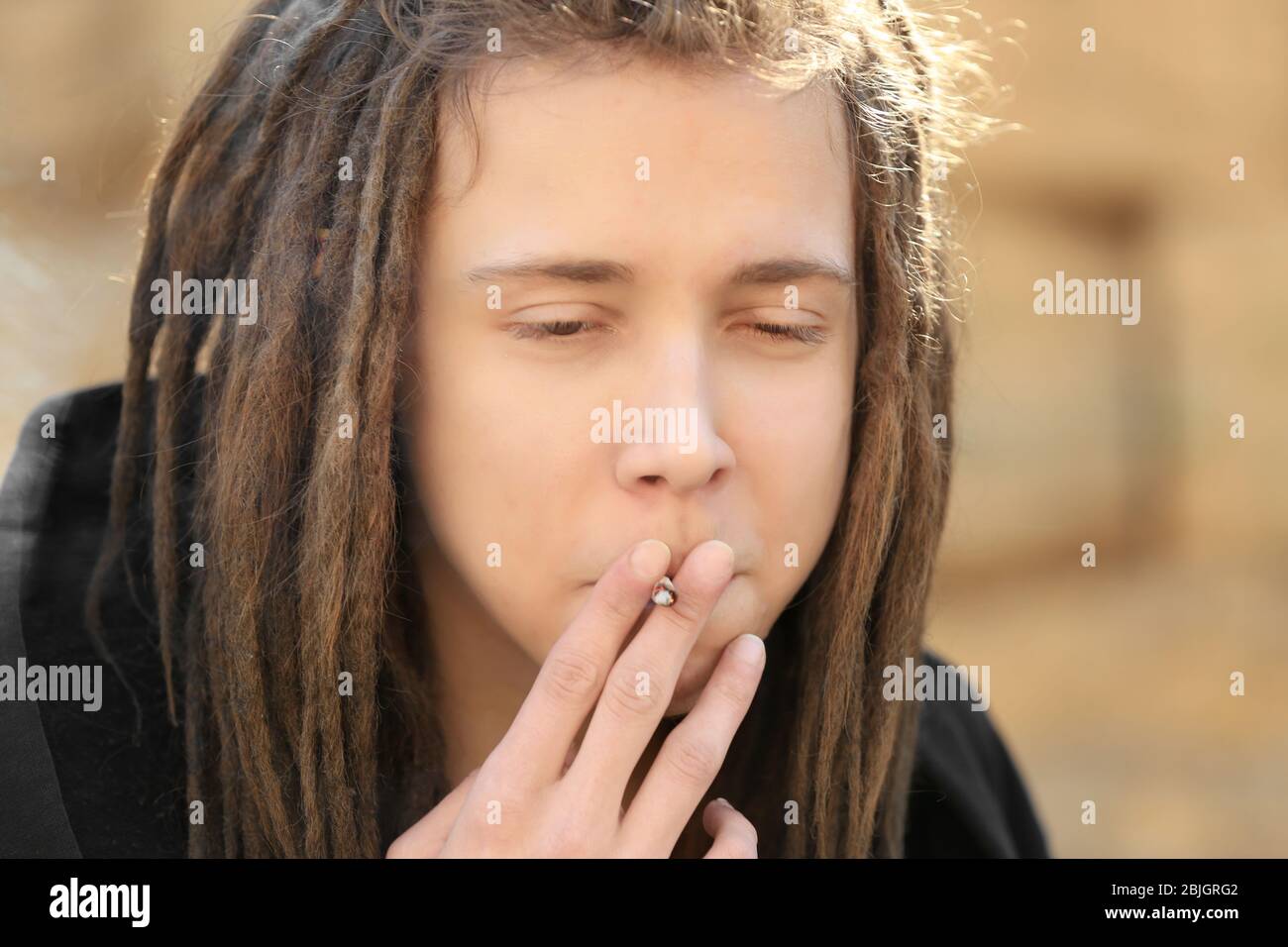 Giovane ragazzo che fuma erbacce su sfondo sfocato Foto Stock