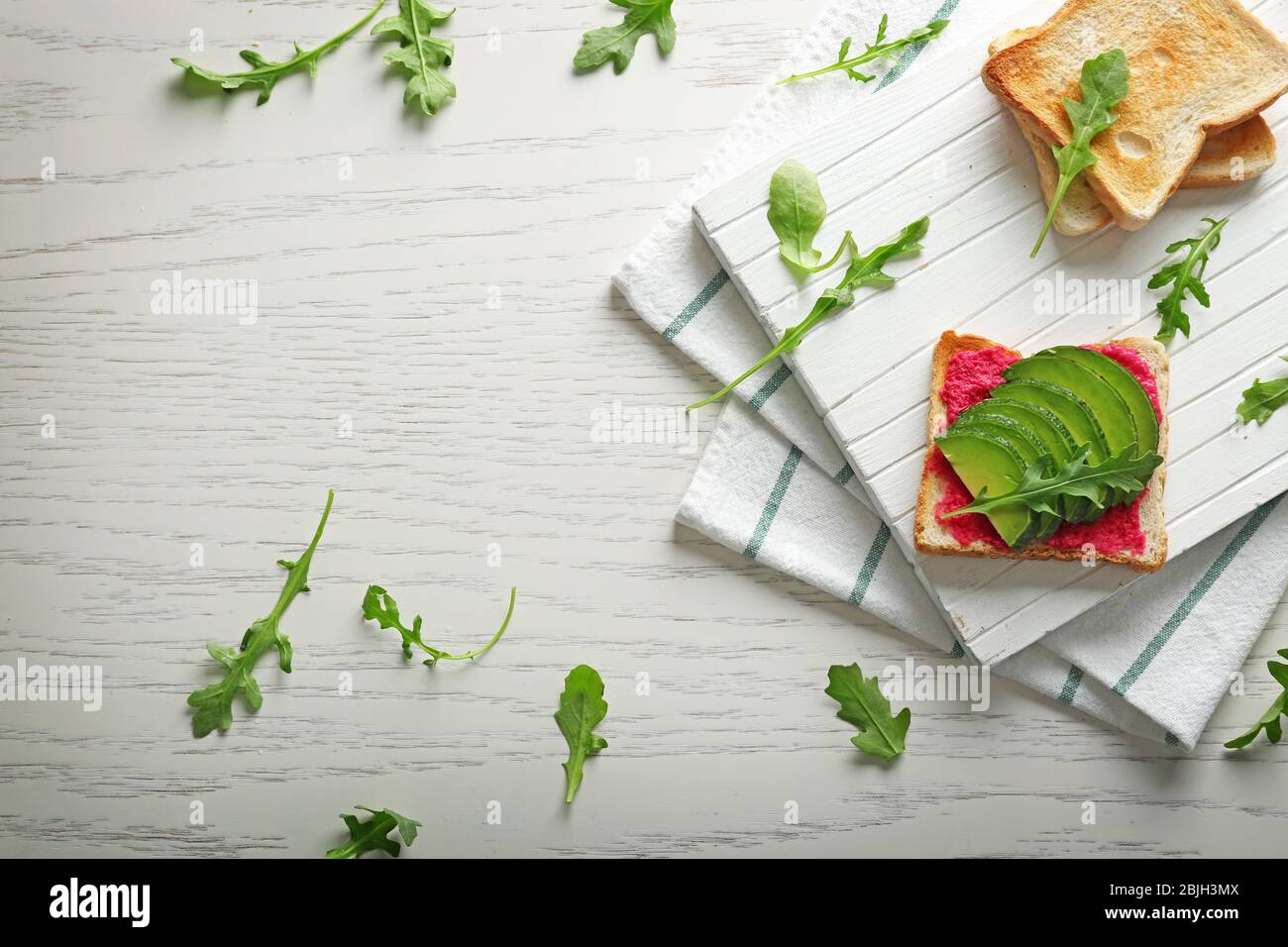 Delizioso toast piccante con avocado e rucola su tavolo di legno bianco Foto Stock