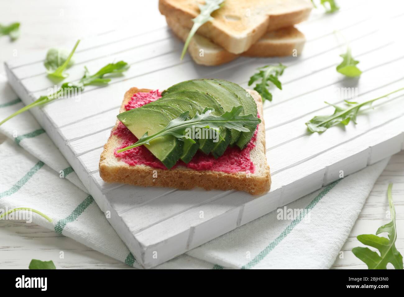 Delizioso toast piccante con avocado e rucola su tagliere bianco Foto Stock
