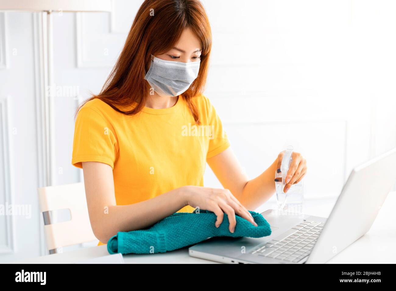 donna che usa e applica gel di alcol per pulire le mani e il laptop a casa Foto Stock