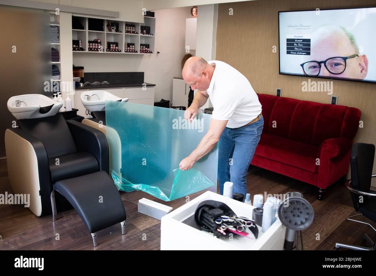 Amburgo, Germania. 27 aprile 2020. Birger Kentzler, presidente dell'associazione della corporazione dei parrucchieri di Amburgo, installa una guardia plexiglas tra i lavandini dei capelli nel suo salone. I parrucchieri hanno dovuto chiudere per sei settimane a causa del nuovo virus corona, e ora saranno autorizzati ad aprirsi di nuovo il 4 maggio. Credit: Christian Charisius/dpa/Alamy Live News Foto Stock