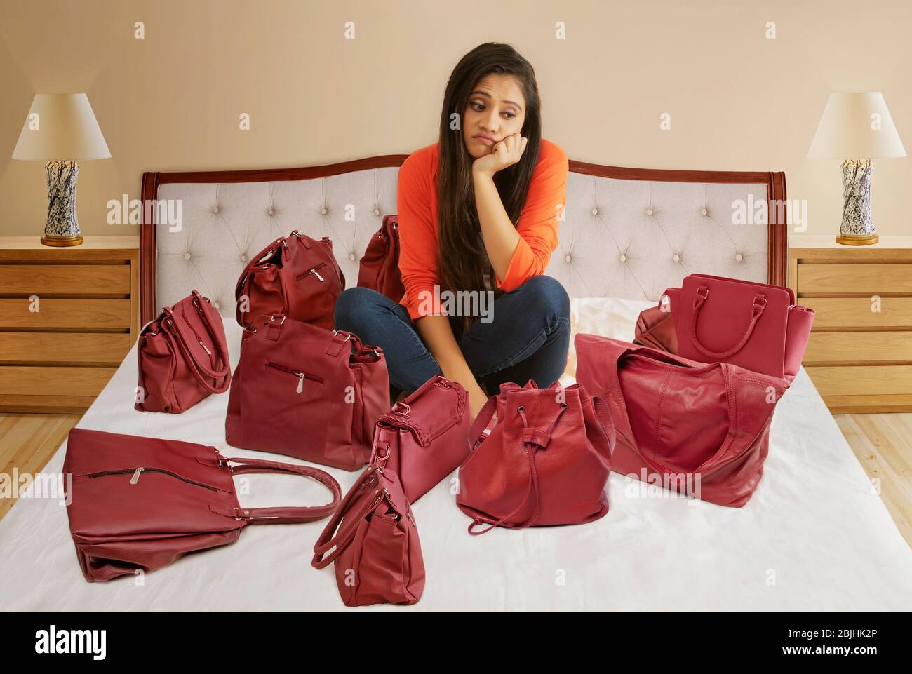 Ragazza seduta a letto con le stesse borse colur con faccia disaapointed Foto Stock