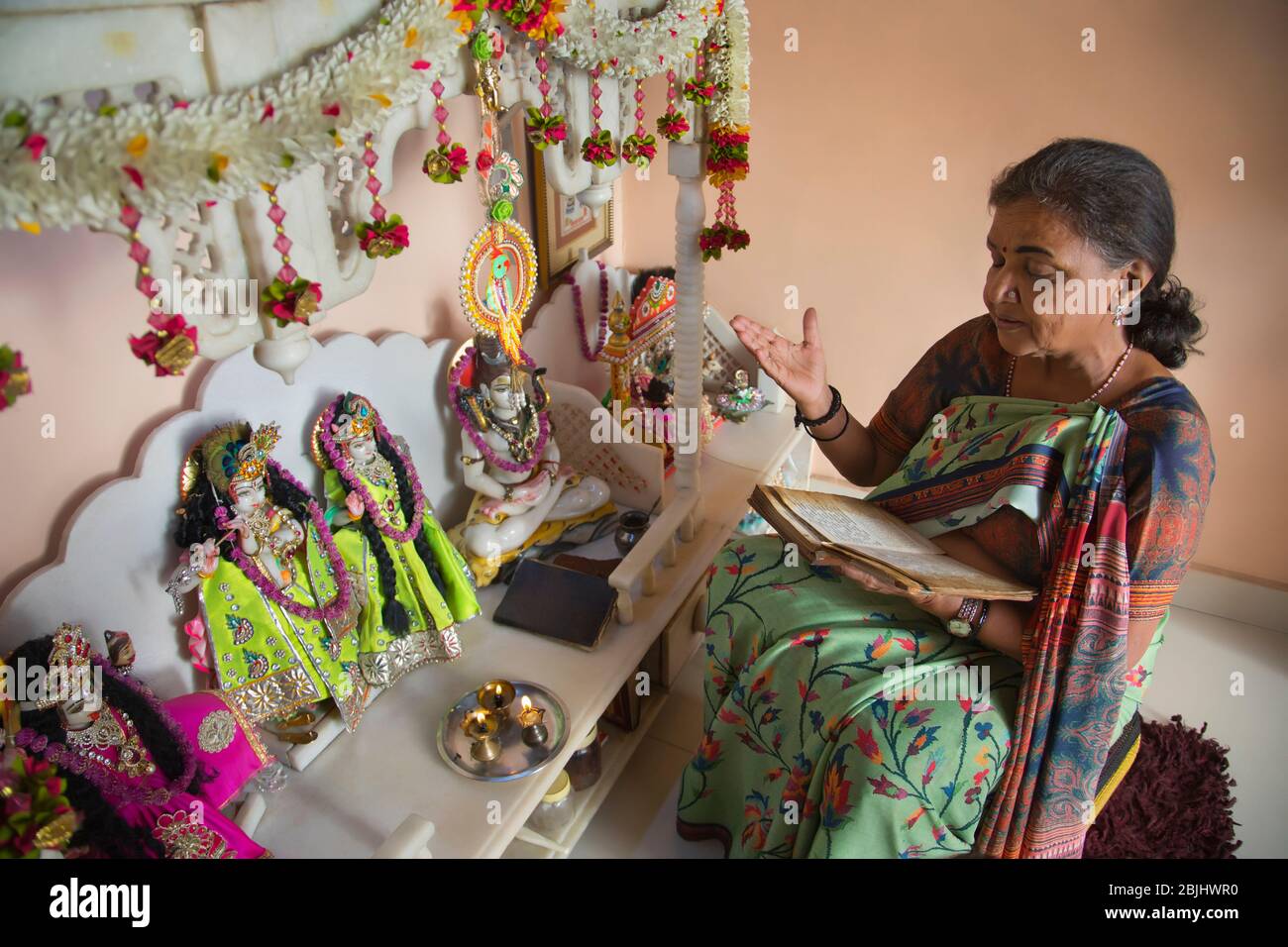 Donna anziana recita preghiere durante la puja a casa. Foto Stock