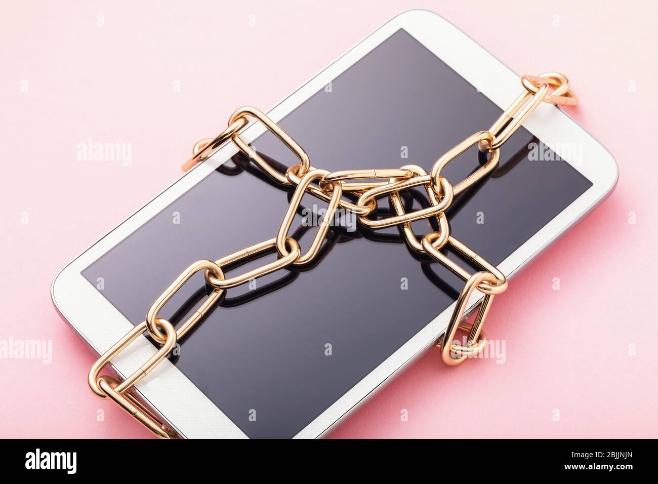 Tablet digitale avvolto in una catena su uno sfondo rosa. Il concetto di non divulgazione dei dati personali Foto Stock