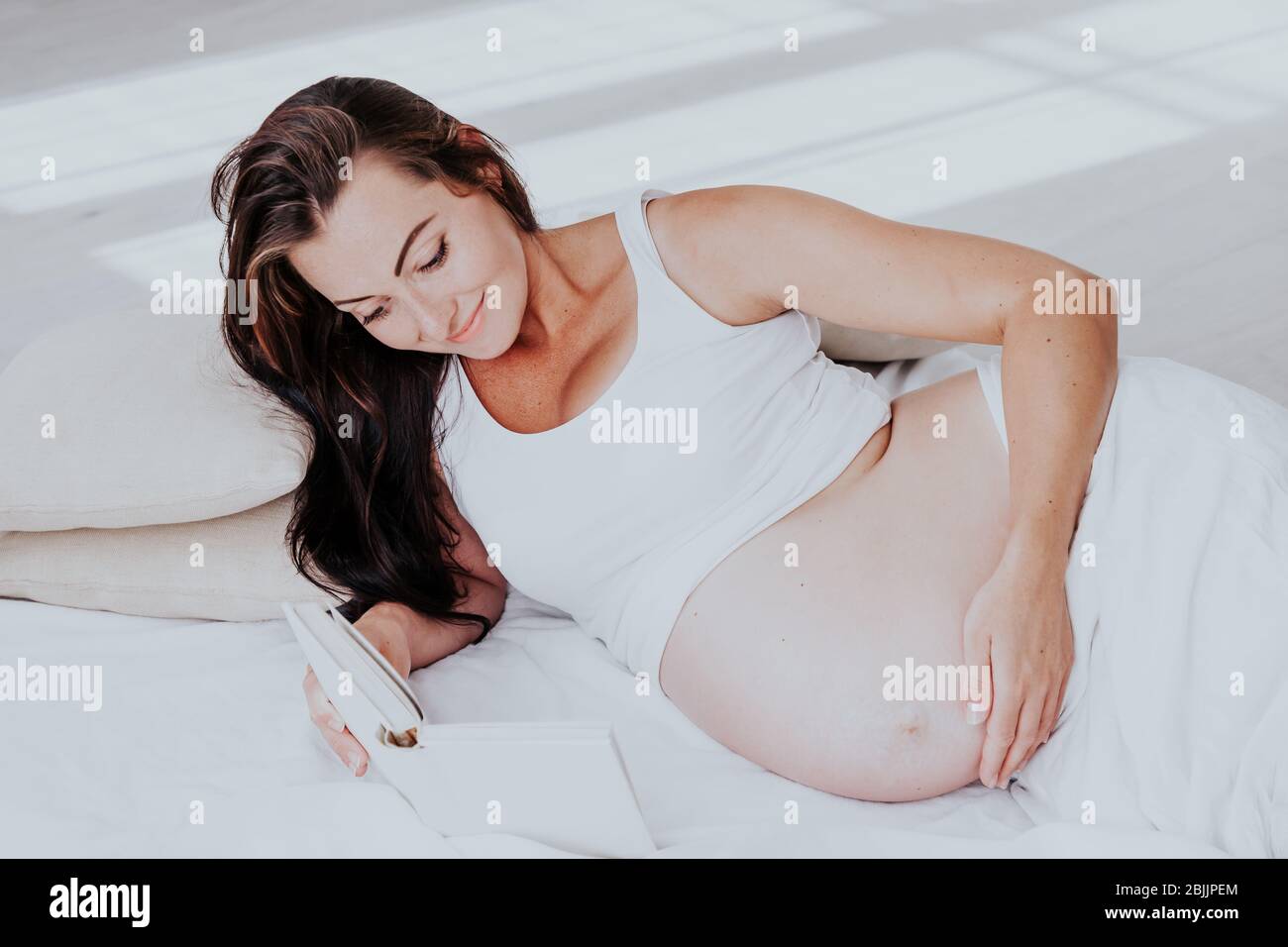 Una donna incinta si trova su un letto e la lettura di un libro Foto Stock