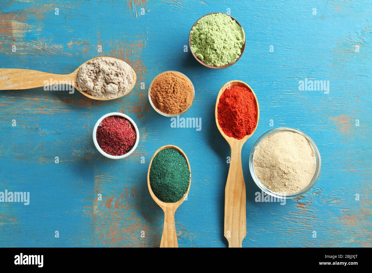 Utensili da cucina con diverse polveri di superfood colorate su tavolo di legno Foto Stock