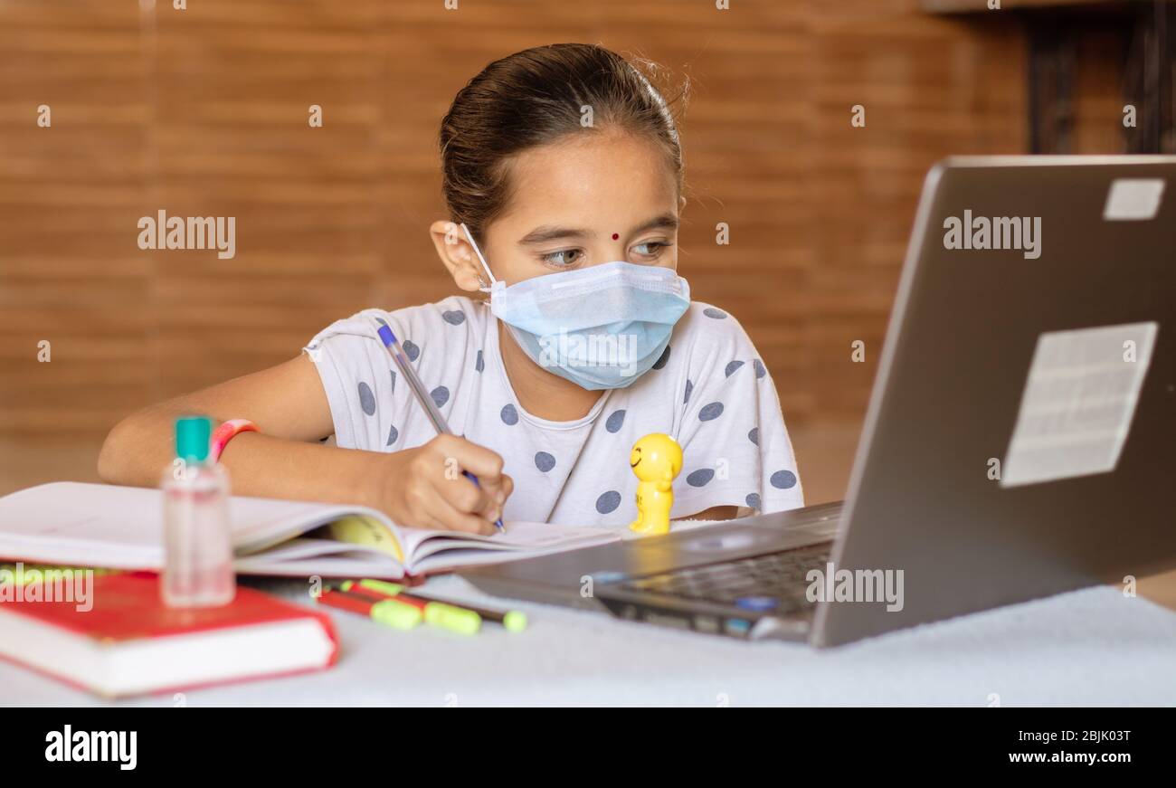 Concetto di homeschooling e e-learning, giovane ragazza con maschera medica scrivendo guardando nel laptop durante il covid-19 o coronavirus pandemic blocco Foto Stock