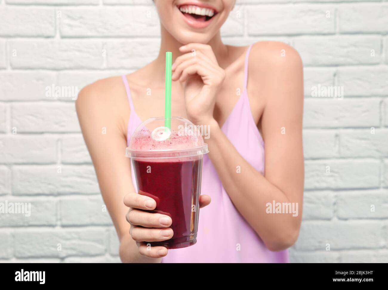 Bella giovane donna con frullato fresco su sfondo bianco muro di mattoni Foto Stock