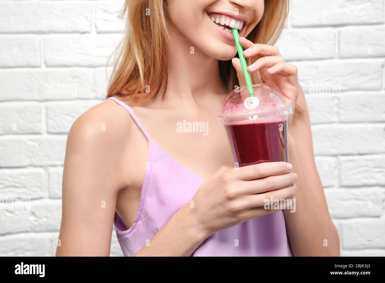 Bella giovane donna con frullato fresco su sfondo bianco muro di mattoni Foto Stock