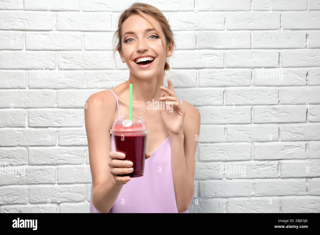 Bella giovane donna con frullato fresco su sfondo bianco muro di mattoni Foto Stock