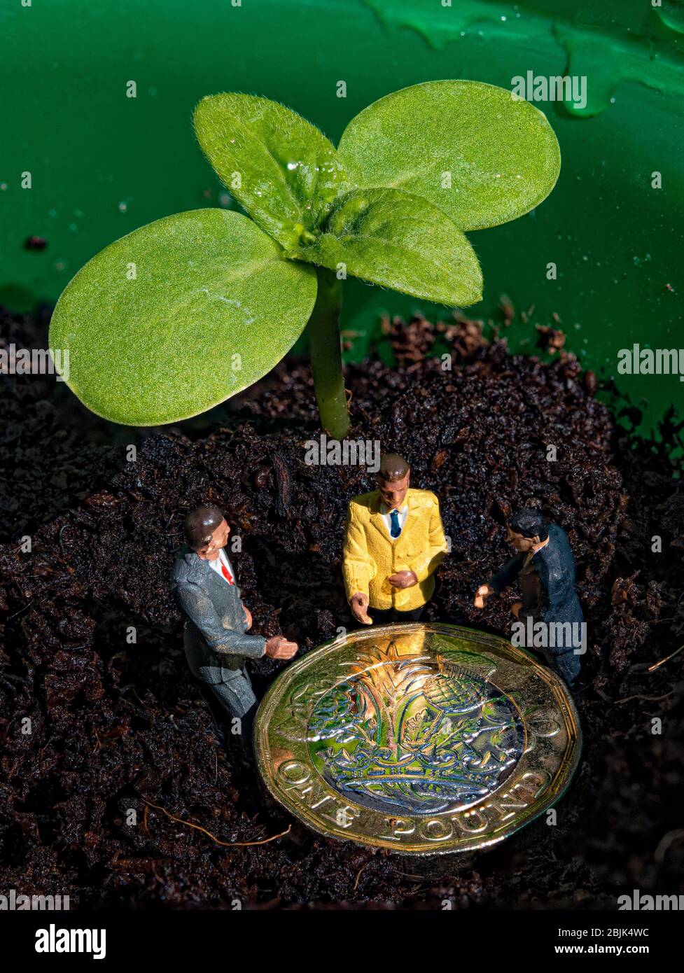 Un nuovo sparo verde con una moneta da libbra e 3 figurine in miniatura su uno sfondo di suolo Foto Stock