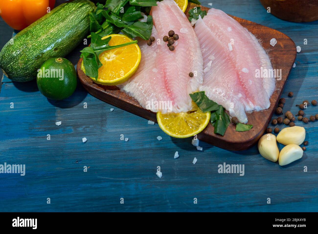 Filetto di pesce con arancia, sale di grano, pepe e spinaci, su una base di legno blu, pronto per cucinare. Foto Stock